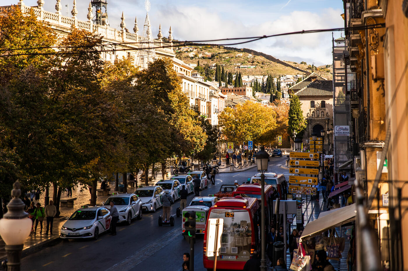 Plaza Nueva a media mañana, desde el balcón de nuestra Suite Plaza Nueva: taxis en fila, un microbús rojo con el letrero C32 y un panel amarillo de señalización hotelera que indica «Zona Cra. del Darro-Albaicín», con la ladera del Albaicín al fondo.
